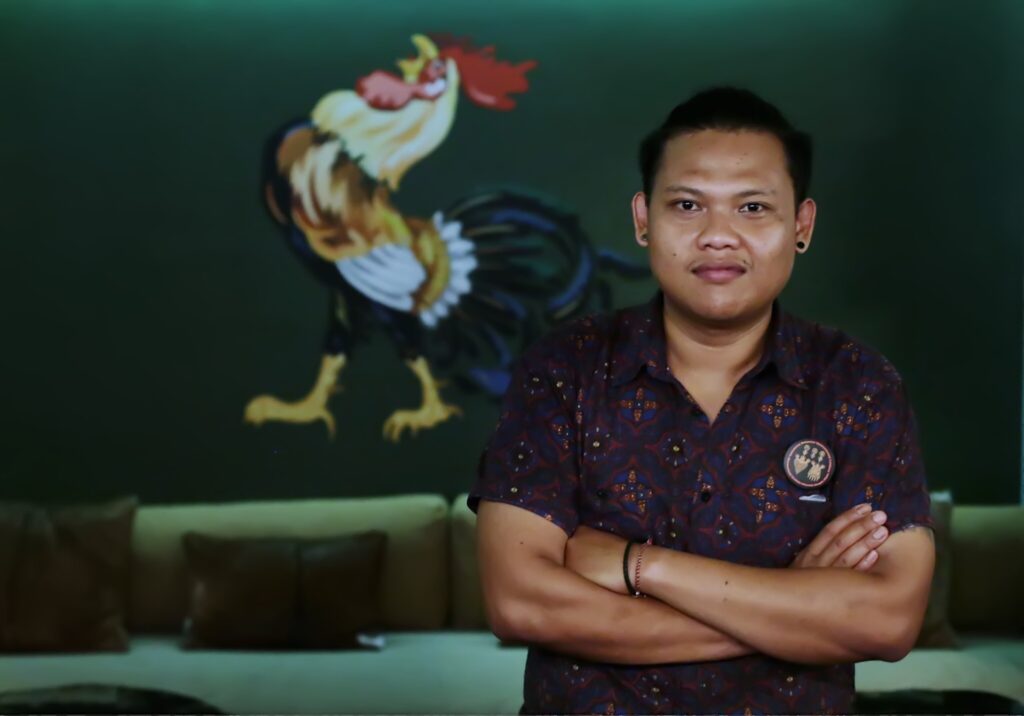 An Indonesian man poses with his arms crossed and a rooster logo appears in the background